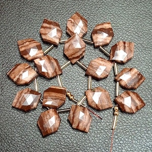 Pode incluir: Um fio de contas de pedras preciosas marrons e brancas com uma forma geométrica facetada. As contas são enfiadas em um fio de ouro com pequenos espaçadores dourados entre cada conta.