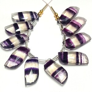 May include: A strand of purple and white striped fluorite gemstone beads. The beads are faceted and have a smooth, polished finish. The beads are strung on a silver wire with gold spacers.
