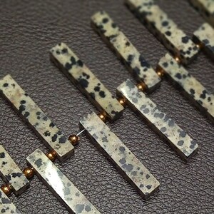 May include: A close-up of a string of brown and black speckled stone beads separated by gold spacers. The beads are rectangular in shape and have a natural, rough texture.