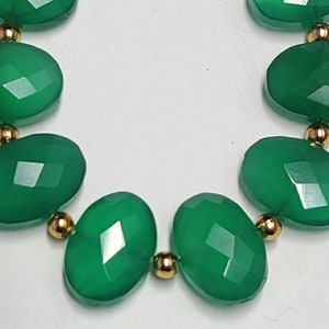 Puede incluir: Un collar de piedras preciosas verdes con cuentas de forma ovalada y separadores dorados.