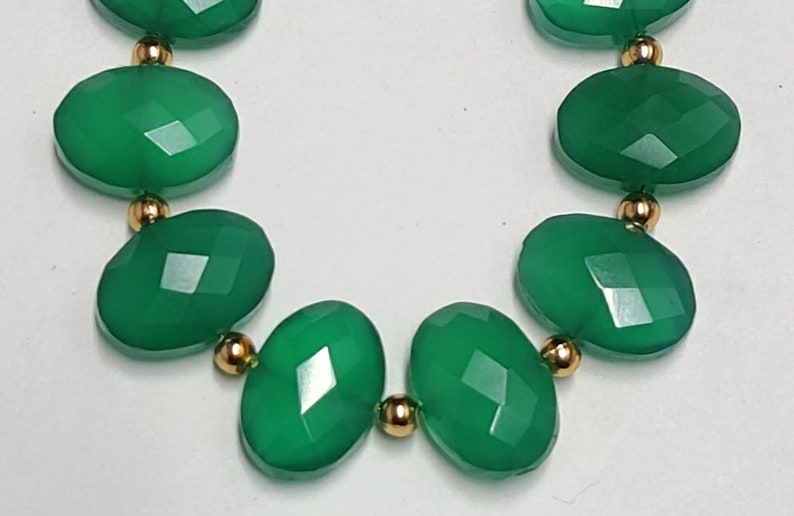 Puede incluir: Un collar de piedras preciosas verdes con cuentas de forma ovalada y separadores dorados.