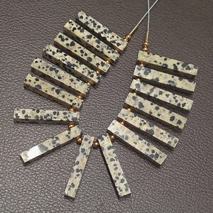 May include: A strand of dalmatian jasper beads, each bead is a rectangular shape with a light brown base and black spots. The beads are strung on a silver wire with gold spacers between each bead.