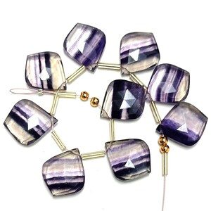 May include: A strand of purple and white fluorite gemstone beads with gold spacers. The beads are faceted and have a teardrop shape.