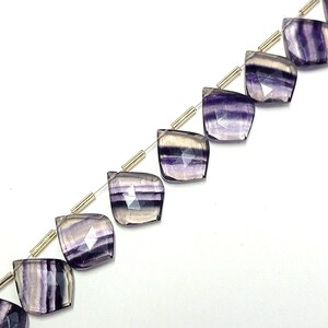 May include: A strand of purple and white striped fluorite gemstone beads. The beads are faceted and have a teardrop shape. The beads are strung on a silver wire with gold spacers.
