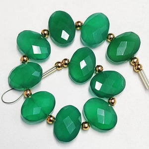 Puede incluir: Una hebra de cuentas de piedras preciosas verdes con detalles dorados. Las cuentas son de forma ovalada y tienen un acabado facetado.