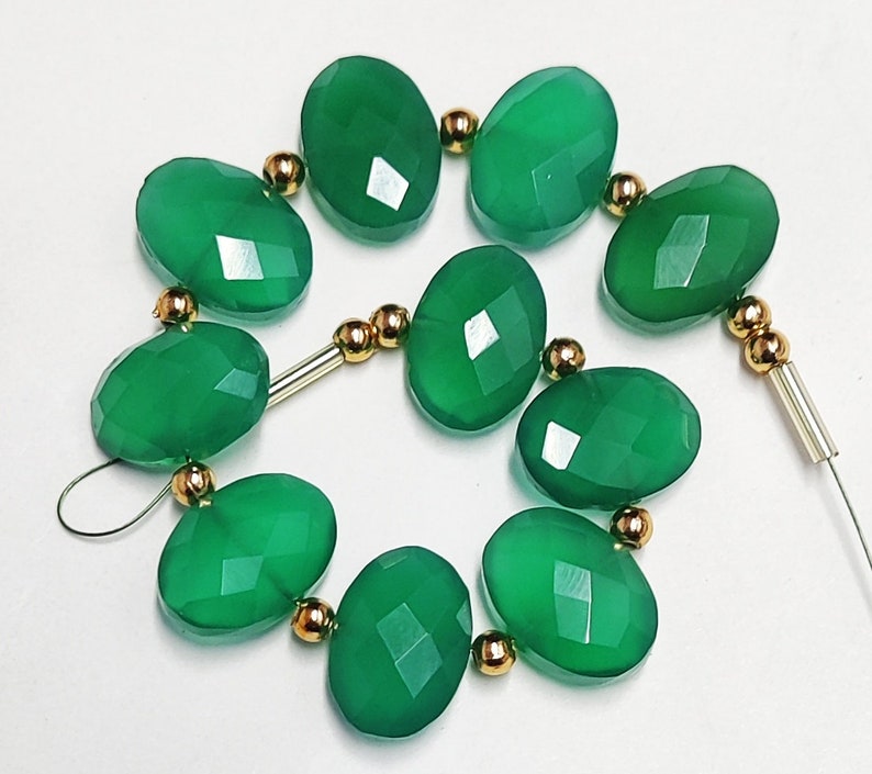 Puede incluir: Una hebra de cuentas de piedras preciosas verdes con detalles dorados. Las cuentas son de forma ovalada y tienen un acabado facetado.