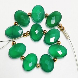 Puede incluir: Una hebra de cuentas de piedras preciosas verdes con separadores dorados. Las cuentas son de forma ovalada y tienen un acabado facetado.