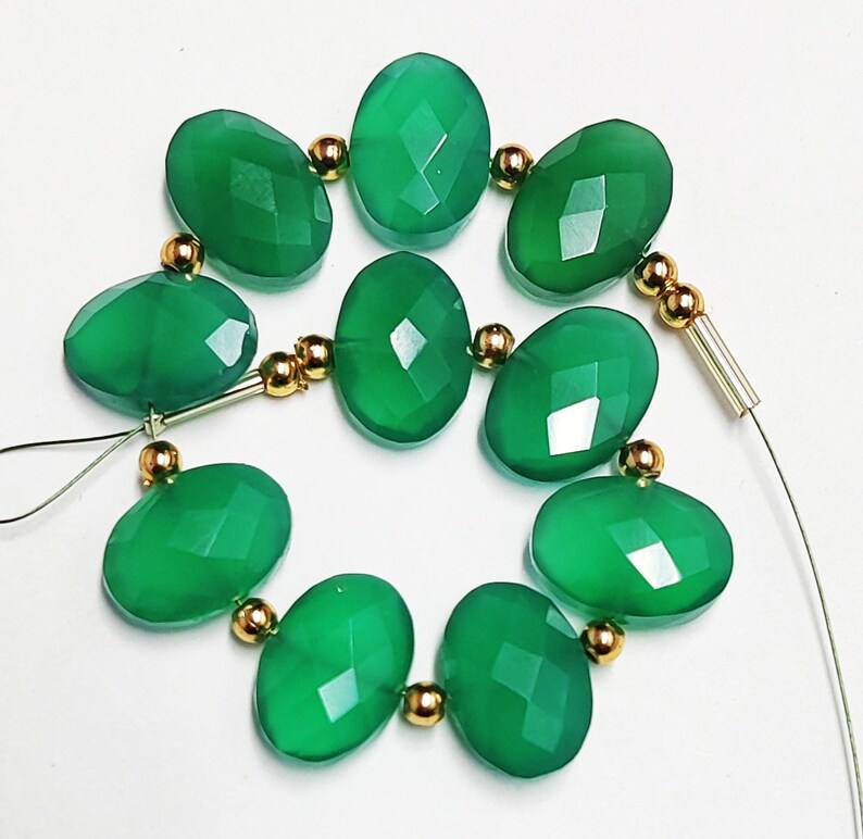 Puede incluir: Una hebra de cuentas de piedras preciosas verdes con separadores dorados. Las cuentas son de forma ovalada y tienen un acabado facetado.
