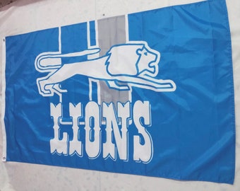 May include: A blue and white flag with a white lion running to the right and the word "LIONS" in white letters below the lion.