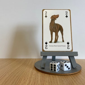 Op de afbeelding: Een houten ezel met een speelkaart waarop een Duitse Kortharige Pointer staat afgebeeld en de 2 van schoppen. Twee witte dobbelstenen staan op de basis van de ezel.