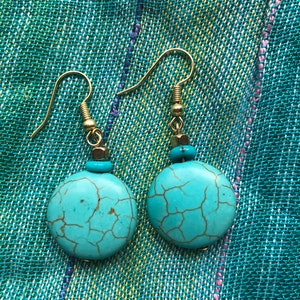 May include: A pair of turquoise blue earrings with gold hooks and a small gold bead accent. The turquoise stones have a cracked or marbled pattern.