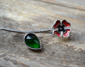May include: A silver poppy brooch with a red enamel flower and a green glass leaf.