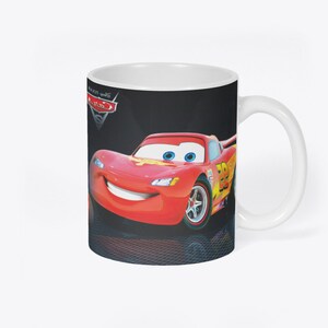 May include: White ceramic mug with a black background featuring a red cartoon race car with a smiling face and blue eyes. The car has the number 95 on the side and the words "Disney Pixar Cars" are visible in the top left corner.