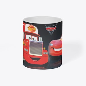 May include: A red and black ceramic mug with a picture of two cartoon cars from the Disney Pixar movie Cars. The cars are smiling and the text "Disney Pixar Cars" is visible on the mug.
