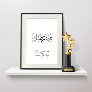 May include: A black framed print with Arabic calligraphy and the text "So patience is most fitting". The print is on a white shelf with a gold star-shaped award.