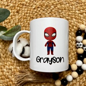 May include: White ceramic mug with a cartoon image of Spiderman in red and blue, and the name Grayson printed in black below the image.