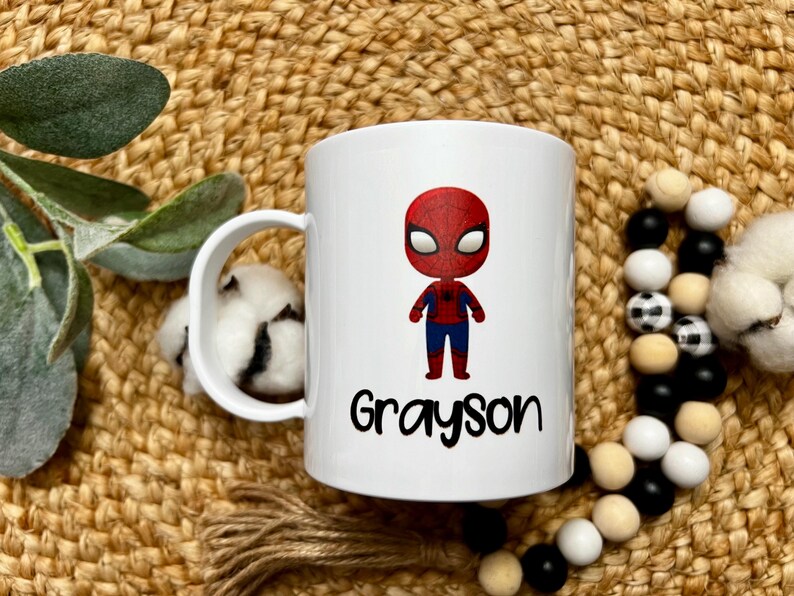 May include: White ceramic mug with a cartoon image of Spiderman in red and blue, and the name Grayson printed in black below the image.