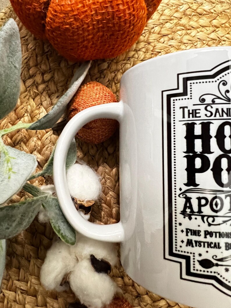May include: White ceramic mug with a black and white graphic design that says "The Sanderson Sisters'  Hot  Potion Apothecary" with the text "Fine Potions & Mystical Brews" at the bottom.