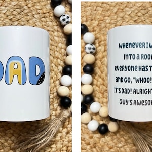 May include: A white ceramic mug featuring the word DAD in blue and yellow bubble letters on one side. The other side displays the black printed text: WHENEVER I WALK INTO A ROOM, EVERYONE HAS TO CLAP AND GO, WHOO! YEAH! IT'S DAD! ALRIGHT! THAT GUY'S AWESOME!