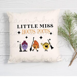 May include: A white pillow with the text "Little Miss Hocus Pocus" and three cartoon characters with broomsticks. The characters are purple, orange, and yellow.