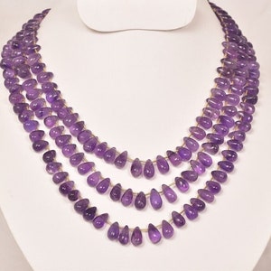 Puede incluir: Un collar de varias hileras hecho con cuentas de piedra preciosa amatista. Las cuentas son facetadas y tienen forma de lágrima. El collar está enhebrado en una cadena dorada.