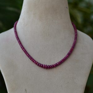 Puede incluir: Un collar hecho de pequeñas cuentas redondas de color rojo rubí.