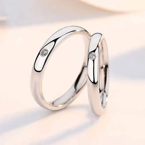 May include: Two silver wedding bands with a single small diamond set in each band.