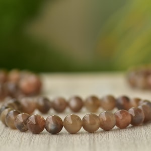 May include: A brown sunstone beaded bracelet with a natural, earthy look. The bracelet is made of round beads and is strung on a stretchy cord.