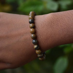May include: A brown and black beaded bracelet with a tiger's eye pattern.