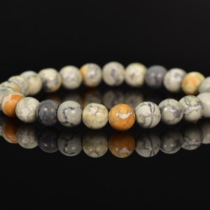 K&ouml;nnte beinhalten: Ein Armband aus runden, mehrfarbigen, nat&uuml;rlichen Steinperlen. Die Perlen sind eine Mischung aus Grau, Wei&szlig; und Orange.