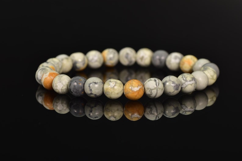 K&ouml;nnte beinhalten: Ein Armband aus runden, mehrfarbigen, nat&uuml;rlichen Steinperlen. Die Perlen sind eine Mischung aus Grau, Wei&szlig; und Orange.
