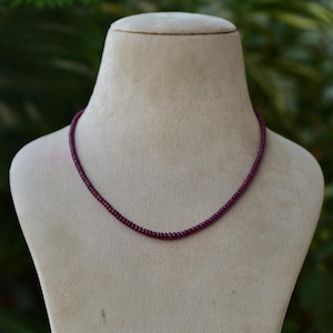 Op de afbeelding: Een delicate ketting gemaakt van kleine, dieprode robijn kralen. De ketting wordt getoond op de nek van een mannequin.