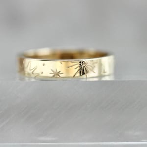 May include: A gold band ring with a starburst design and small stars engraved around the band.