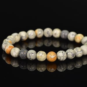 K&ouml;nnte beinhalten: Ein Armband aus runden, mehrfarbigen Steinen. Die Steine sind eine Mischung aus Wei&szlig;, Grau und Orange.