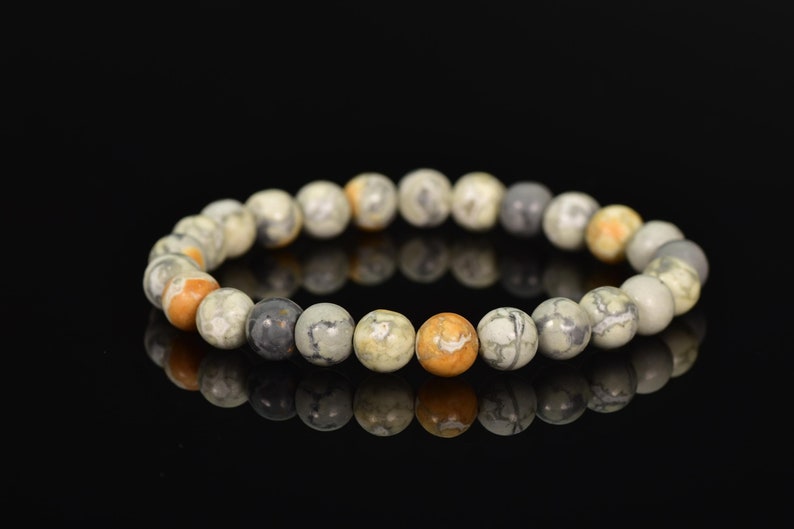 K&ouml;nnte beinhalten: Ein Armband aus runden, mehrfarbigen Steinen. Die Steine sind eine Mischung aus Wei&szlig;, Grau und Orange.