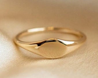 Puede incluir: Un anillo de sello de oro con una parte superior lisa de forma ovalada.