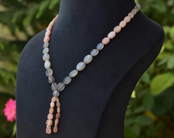 May include: A necklace made of oval-shaped sunstone beads. The beads are a gradient of grey and pink. The necklace has a tassel at the bottom.
