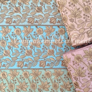 May include: Two rolls of gold embroidered trim with floral patterns. One roll is on a light blue background and the other is on a light pink background. The trim is labeled "Emb1120".