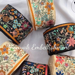 May include: Assortment of six embroidered trim ribbons with floral designs in various colors, including black, white, orange, pink, and blue. The trim is perfect for adding a touch of elegance to clothing, home decor, and crafts. The text "Emb1221" is visible in the bottom left corner of the image.