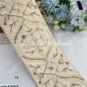 May include: White fabric trim with gold embroidery and sequins. The trim features a repeating pattern of floral designs and geometric shapes. The trim is labeled "Emb1222 #4".