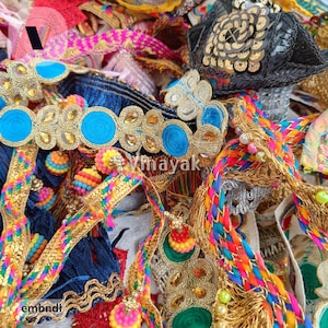 Op de afbeelding: Assortiment van kleurrijke bies en versieringen, waaronder goud, blauw en roze, met kwastjes en franjes. De bies zijn perfect om kleding, woonaccessoires en knutselwerk een vleugje glans en textuur te geven.