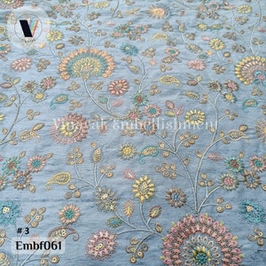May include: A light blue fabric with a floral embroidery pattern. The flowers are in shades of pink, yellow, and green. The fabric has a subtle sheen and a delicate texture.