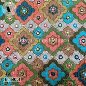 May include: A fabric with a repeating pattern of colorful floral designs. The fabric is embroidered with sequins and small mirrors. The fabric is beige with shades of pink, blue, green, and gold.