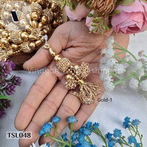 May include: Gold beaded tassel trim with a gold and clear beaded fringe. The trim is shown on a hand with a ring. The trim is labeled "Gold-1" and "TSL048".