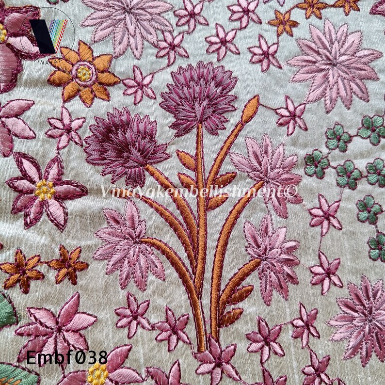 May include: A close-up of a beige fabric with intricate embroidery of pink, orange, and green flowers. The embroidery is detailed and delicate, with a variety of floral patterns. The fabric has a subtle texture and a soft, luxurious feel.
