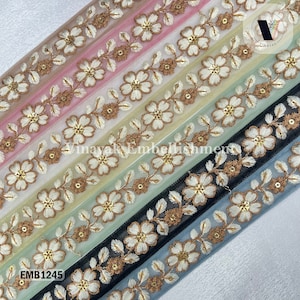 May include: A selection of floral embroidered trim in various colors, including pink, white, green, black, and blue. Each trim features white flowers with gold centers and brown accents. The text "Vinayak Embellishment" and "EMB1245" are visible.