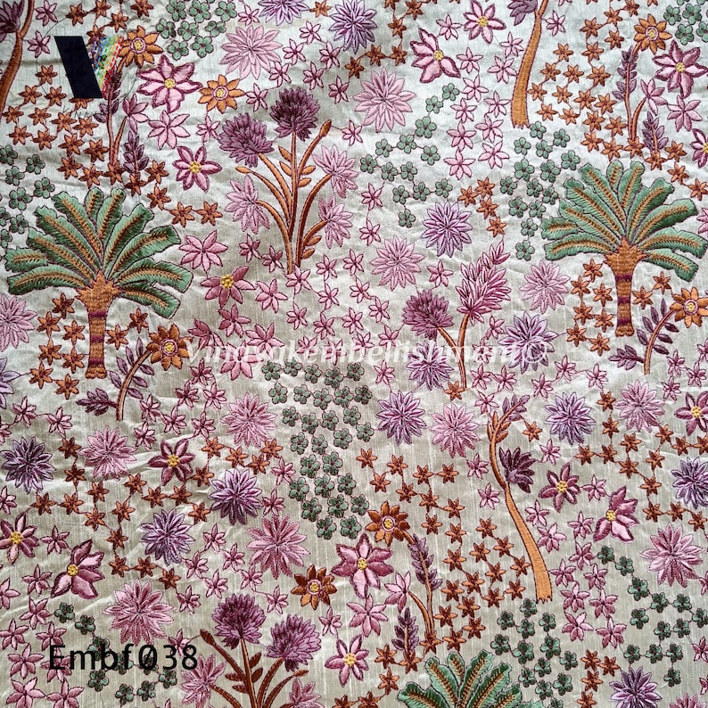 May include: A beige fabric with an embroidered floral pattern. The design features pink, purple, and green flowers, along with palm trees. The fabric has the text "Embf038" in the bottom left corner.