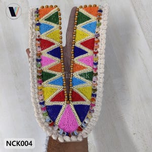 May include: A colorful beaded neckline with a geometric design. The piece features triangles in red, blue, yellow, green, orange, and pink, bordered by cream-colored fabric and wooden beads. The text "NCK004" is visible.