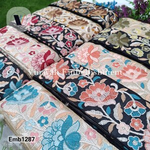 May include: A close-up of several rolls of black embroidered trim with colorful floral designs. The trim is on a beige fabric background. The text "Emb1287" is visible in the bottom left corner of the image.