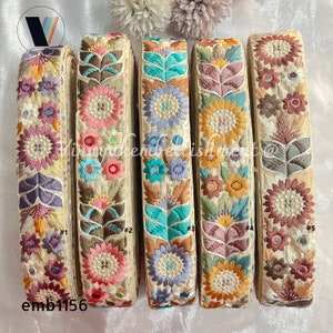 May include: Five spools of embroidered trim with floral designs in shades of pink, blue, green, and brown. The trim is on a cream background. The spools are labeled #1 through #5. The text emb1156 is below the spools.